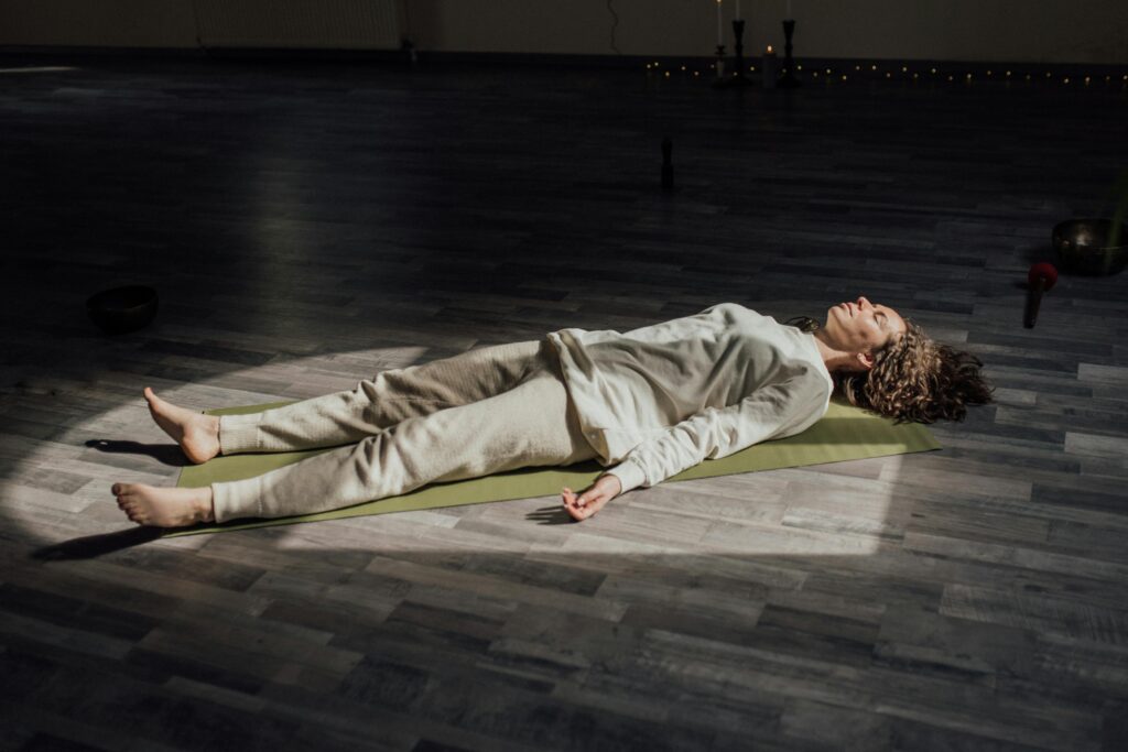 Woman lying on a yoga mat indoors, meditating and relaxing in a calm setting.