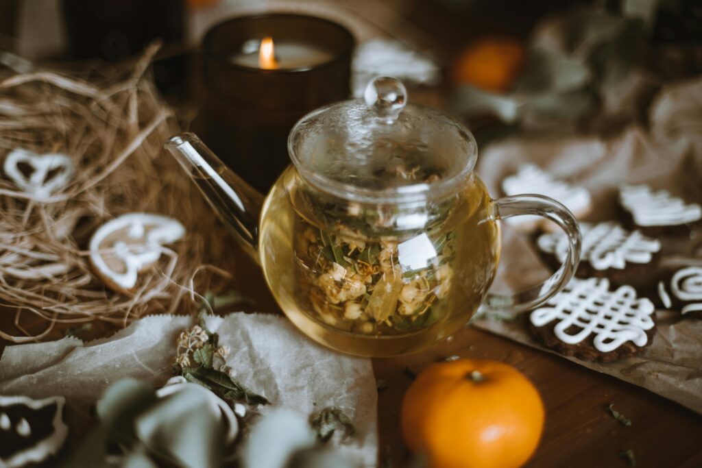 Warm setup with herbal tea in a glass teapot, cookies, and a lit candle, perfect for cozy moments.